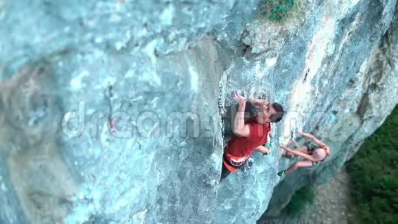 两名攀岩者在艰难的运动路线上攀爬男子在前景上伸手抓住女子则爬上视频的预览图