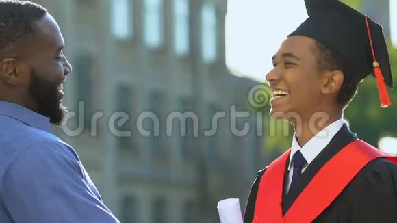 快乐的黑人男子拥抱微笑的儿子穿着官服骄傲的父亲支持视频的预览图
