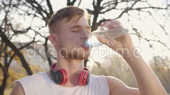 英俊的白人运动员在阳光下喝水的特写肖像在户外运动的小男孩视频的预览图