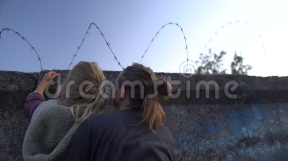 母亲和女儿拥抱着绝望地看着难民营的栅栏视频的预览图