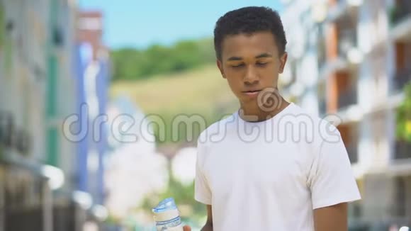 运动疲惫的男性青少年在户外活动后饮用瓶装水视频的预览图