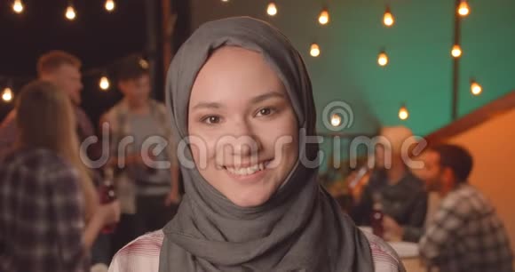 年轻漂亮的穆斯林女性戴着头巾看着镜头在舒适的聚会上开心地微笑着视频的预览图