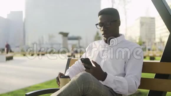严肃的非洲男人坐在公园的长凳上在笔记本上写笔记视频的预览图