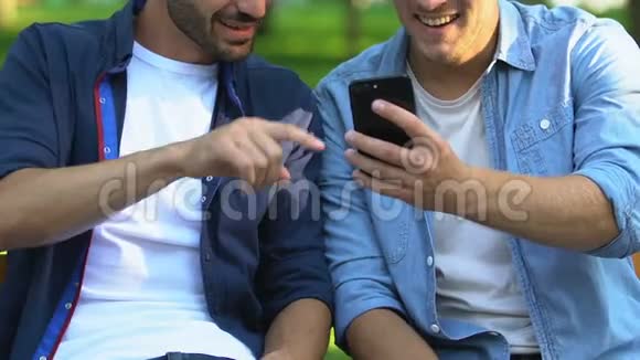 两个朋友坐在公园的长凳上看智能手机上的搞笑视频特写镜头视频的预览图