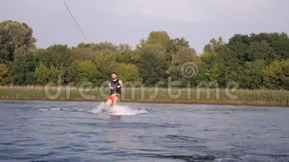 快乐的唤醒者骑在摩托艇后面溅起水花握住绳柄运动员在河边训练视频的预览图