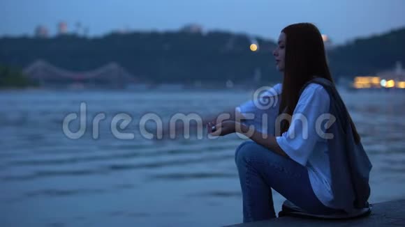 体贴的少女坐在河岸上享受平静的夏日夜晚视频的预览图