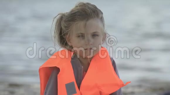 孤独女孩穿着救生衣看着摄像机在紧急情况下的行为视频的预览图