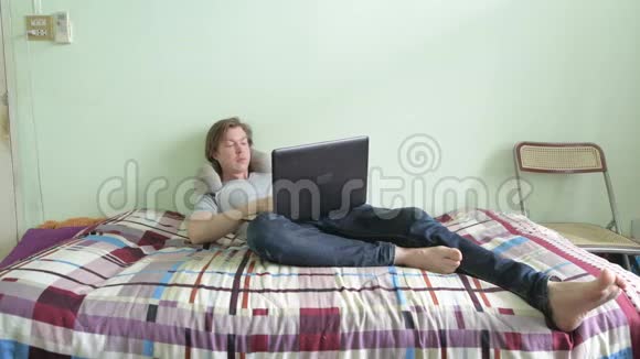 快乐的年轻帅哥在卧室放松时使用笔记本电脑视频的预览图
