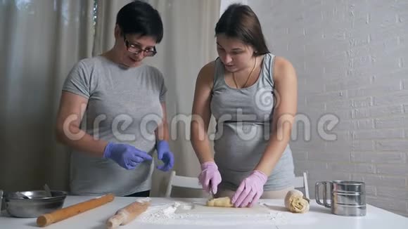 妈妈和怀孕的女儿在家厨房准备饺子和糕点的面团视频的预览图