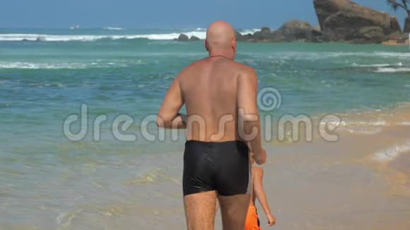 成熟的爸爸在度假胜地阳光沙滩上跟着儿子跑视频的预览图