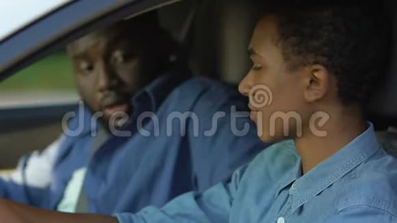 黑人男性告诉青少年在驾驶座上系安全带爸爸教儿子视频的预览图