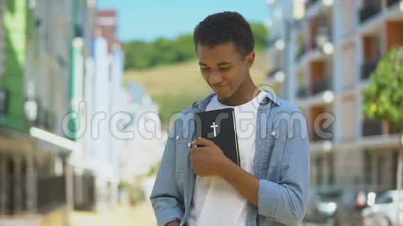 高兴的非裔美国年轻男性拥抱圣经看教堂信仰视频的预览图