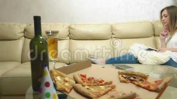 可爱的金发女孩在沙发上看书喝酒吃披萨视频的预览图