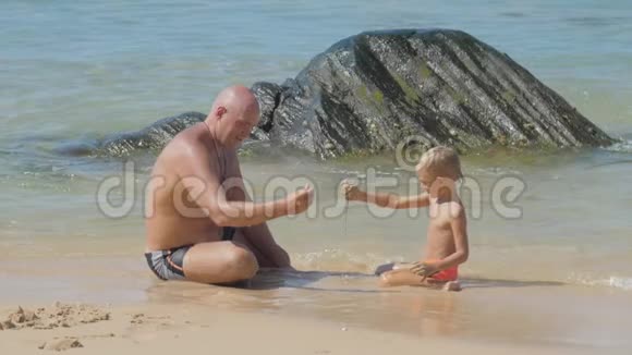 男人和有趣的儿子在沙滩上玩石头视频的预览图