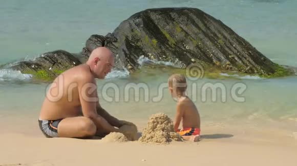 男孩和父亲看着海浪摧毁的沙塔视频的预览图
