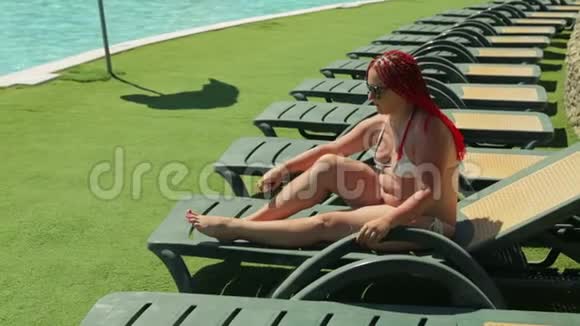 一位现代犹太妇女在泳池边的阳光休息室里用防晒霜涂抹她的身体视频的预览图