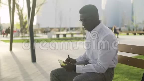 年轻的非裔美国人坐在公园的长凳上把她的想法写在日记里视频的预览图