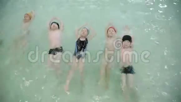孩子们背在游泳池里游泳孩子们戴着漂浮的帽子学会在学校的游泳池里游泳视频的预览图