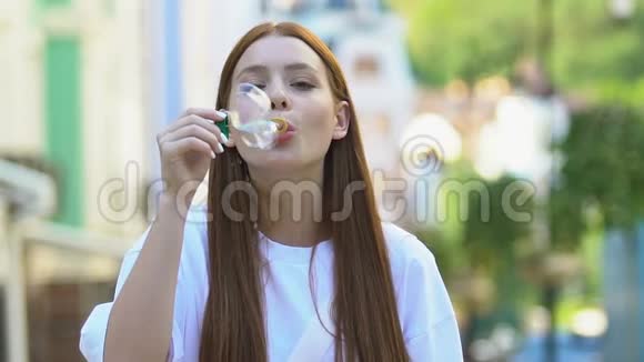 迷人的年轻女性吹着肥皂泡在镜头上微笑慢镜头视频的预览图