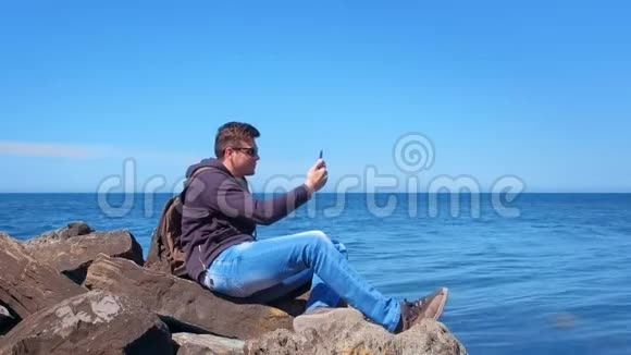 年轻的旅游旅行者在海上坐在巨大的巨石上聊天视频的预览图