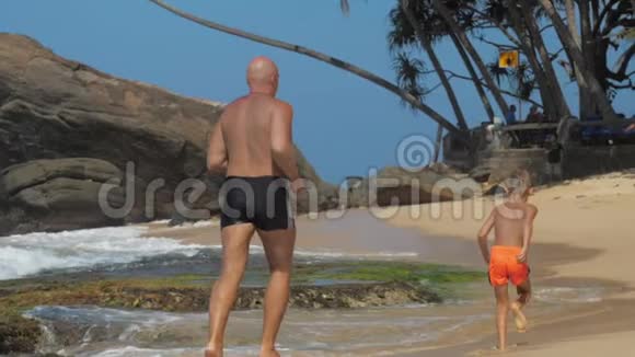 爸爸和儿子玩得很开心沿着热带海滩跑步视频的预览图