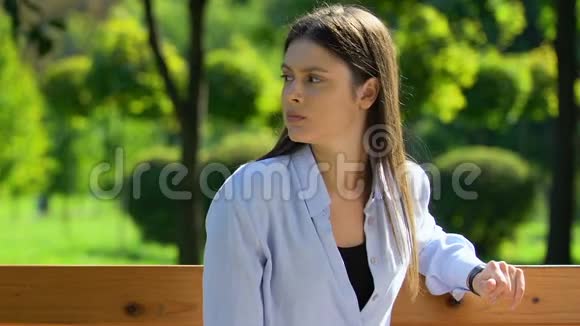 紧张的黑发女人在公园的长凳上等朋友环顾四周开会视频的预览图