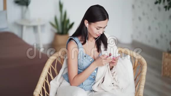戴耳机的年轻女子坐在家里的椅子上用电话上网聊天视频的预览图