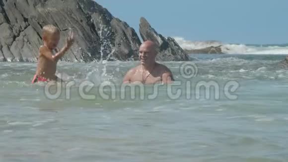 开朗的男人溅起海水在岩石上与儿子嬉戏视频的预览图