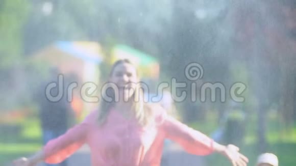 在公园里暑假里无忧无虑的年轻金发碧眼的女孩享受着新鲜的喷泉滴视频的预览图