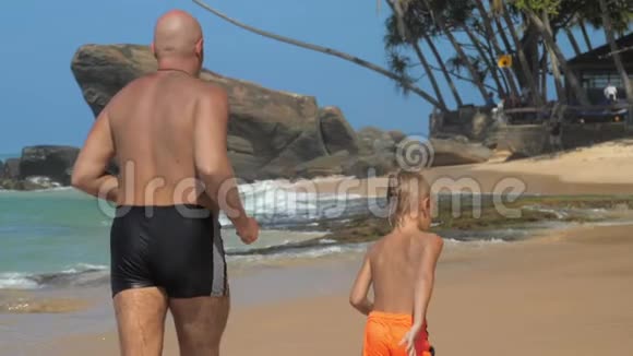 小男孩和爸爸沿着海边的沙滩跑沿着岩石跑视频的预览图
