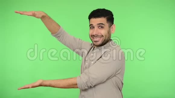 你看这里快乐满意的黑发男人穿着衬衫握着手掌指着复制空间摄影棚绿色背景视频的预览图