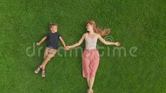 一名年轻女子和她儿子躺在草坪上的空中射击视频的预览图
