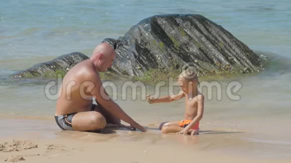 爸爸和可爱的男孩坐在冲浪线上玩湿沙视频的预览图