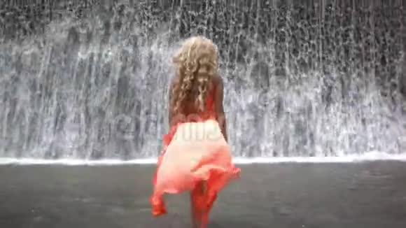 一位穿着橙色衣服的年轻美女正在向大瀑布靠近视频的预览图