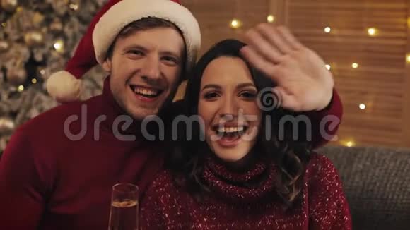 圣诞树附近沙发上的一对年轻白种人夫妇的肖像家庭挥手视频呼叫微笑视频的预览图