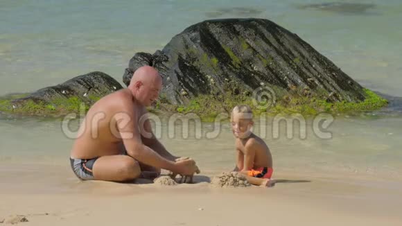 父亲在海洋慢动作中扮演儿子挖湿沙子视频的预览图