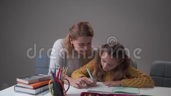 年轻女性高加索家庭教师帮助她的学生做家庭作业的肖像可爱的高加索女孩在练习中写作视频的预览图