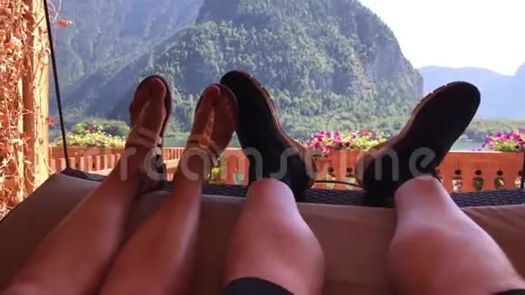 在阳光明媚的山林湖景中第一人拍浪漫的双腿在舒适的鲜花阳台上摆动视频的预览图