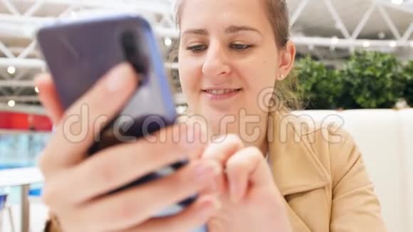 特写4k视频微笑的年轻女子在智能手机上社交媒体上打字同时坐在餐厅视频的预览图