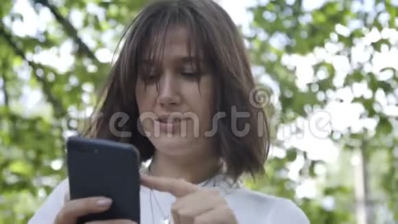 有魅力的女人微笑着在公园或森林里打短信的肖像女人在电话里聊天阅读新闻视频的预览图