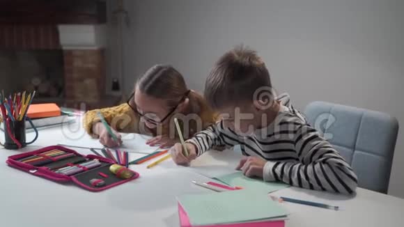 两个白人孩子一起做作业聪明的兄妹在练习本中写作穿条纹衣服的男孩视频的预览图