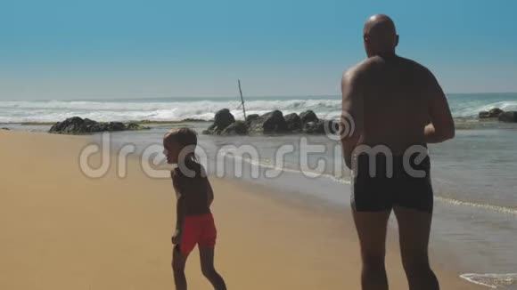 男孩和父亲一起在海边和岩石边跑步视频的预览图