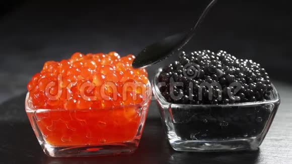 红色和黑色鱼子酱在两个相同的透明玻璃碗上的黑色背景人勺鱼子酱视频的预览图