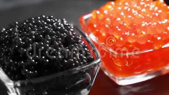 红色和黑色鱼子酱在两个相同的透明玻璃碗上的黑色背景旋转视频一个背景视频的预览图