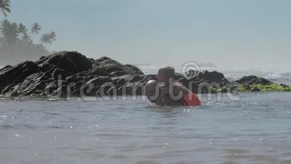 爸爸和小男孩在大海里的大石头后面游泳视频的预览图
