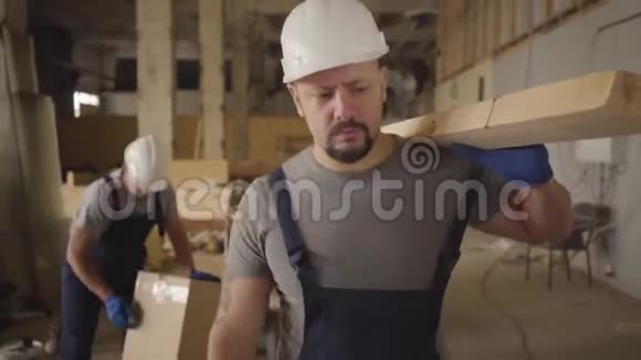 穿着白色头盔和蓝色制服的壮汉在工地上用木板走路挥手视频的预览图