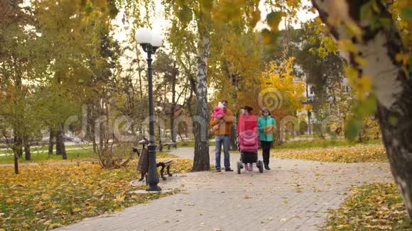 快乐的父母带着一个小宝宝和一个成年的女儿在秋天的公园里散步笑妈妈和爸爸一起玩视频的预览图