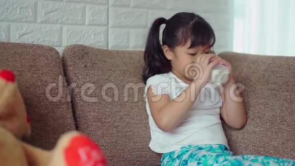 小女孩坐在沙发上用玻璃喝牛奶视频的预览图