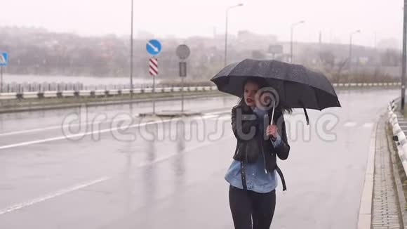 一个悲伤的女孩站在一条空路上的伞下她抓住了车视频的预览图