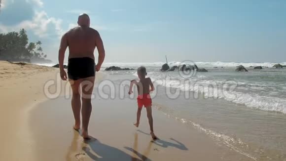父亲和儿子一起沿着海边的海滩和晴朗的天空视频的预览图